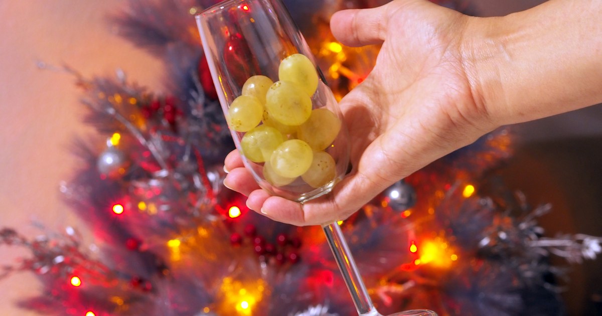 Copa con las doce uvas de Nochevieja delante de un árbol de Navidad